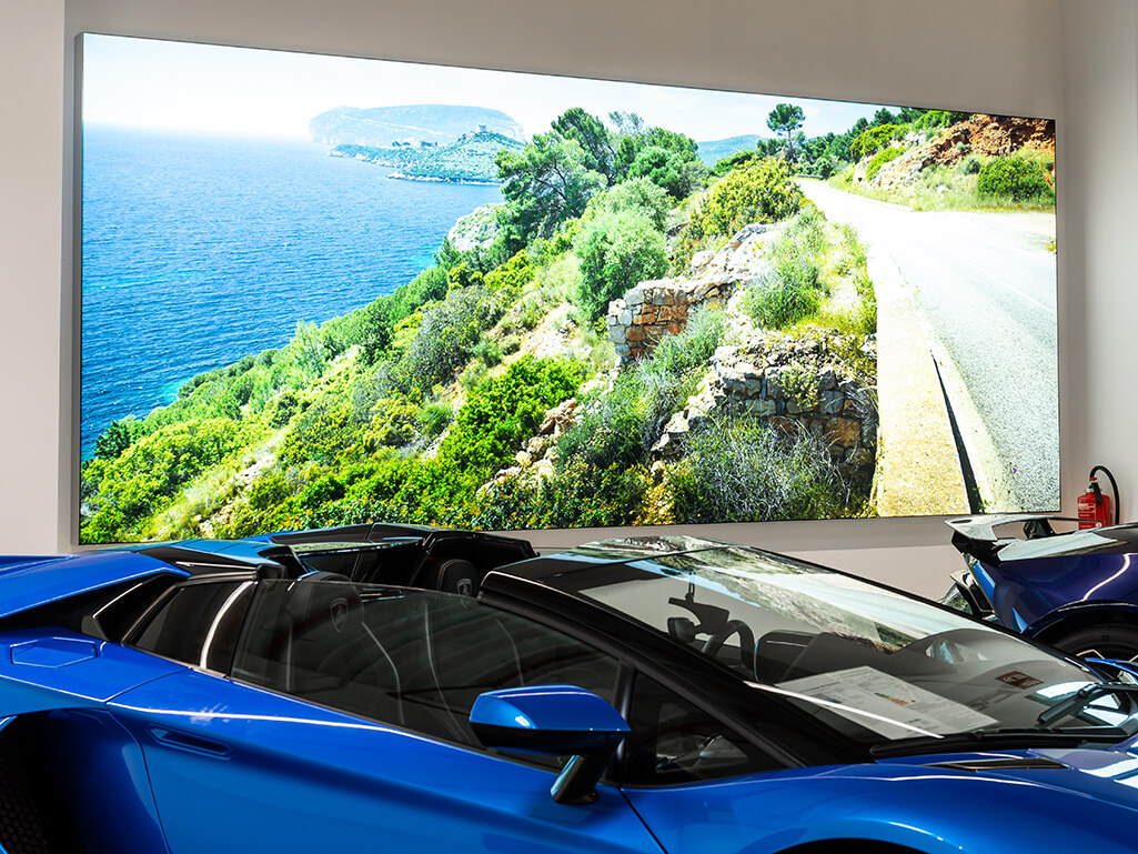 Selbstleuchtende, großformatige Wandbilder mit italienischen Küstenlandschaften in einem Autohaus. Im Vordergrund sind edle italienische Wagen der Marke Lamborghini zu sehen.