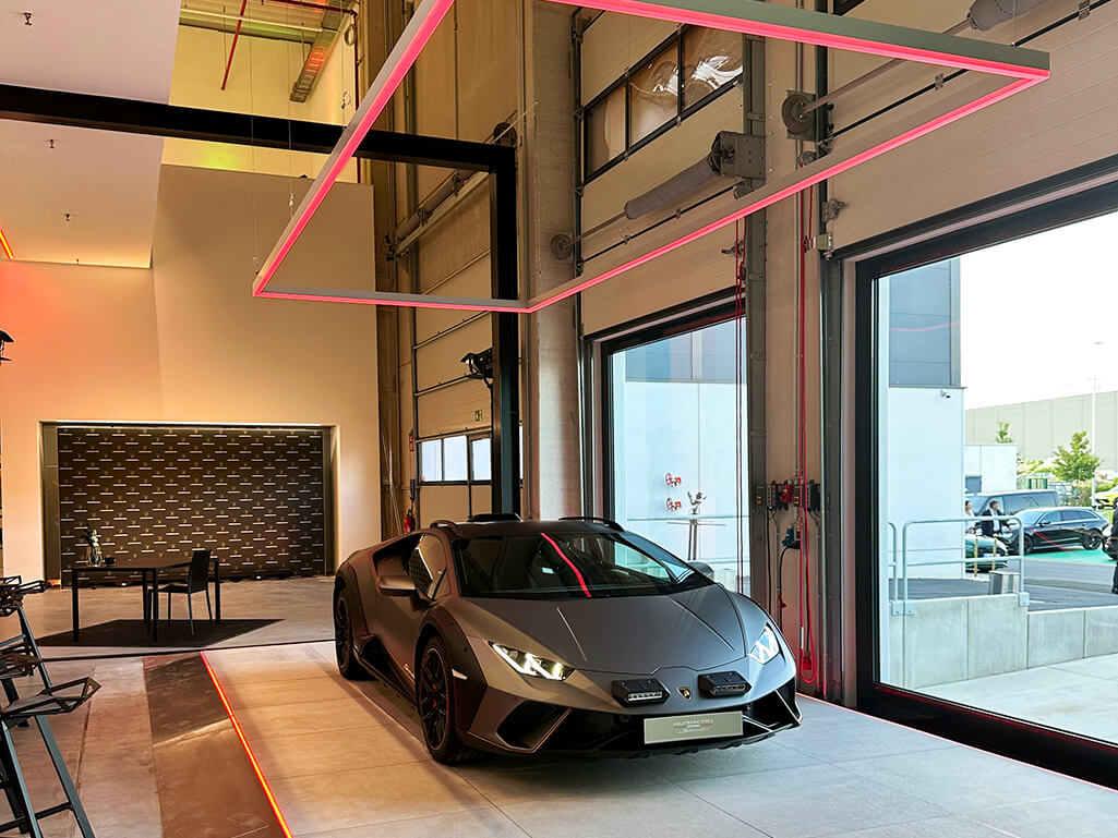 Ein Autohaus. Ein Lamborghini steht steht in einer ACR-Lichtinstallation für Boden und Decke und wird wirkungsvoll mit farbigen Licht angestrahlt.